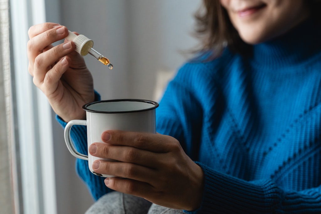 Using a dropper to put a CBD tincture into a mug of tea