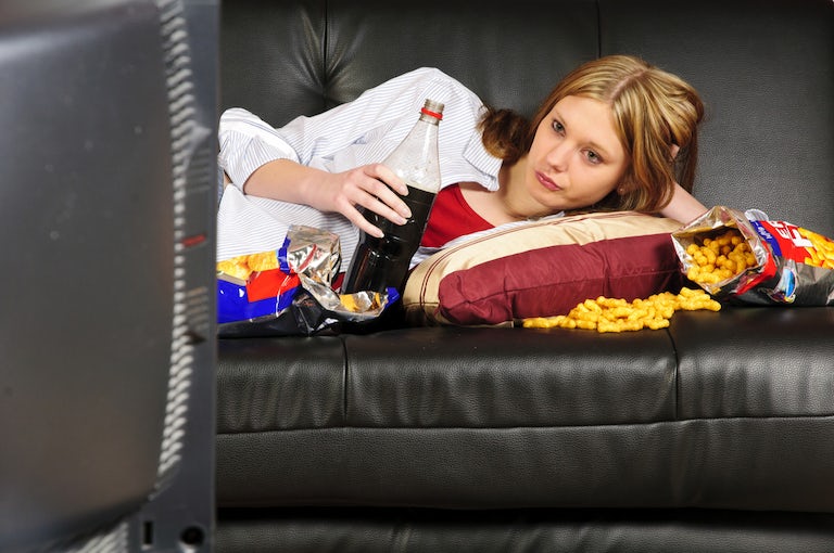 Woman lies on the couch eating food due to have the munchies