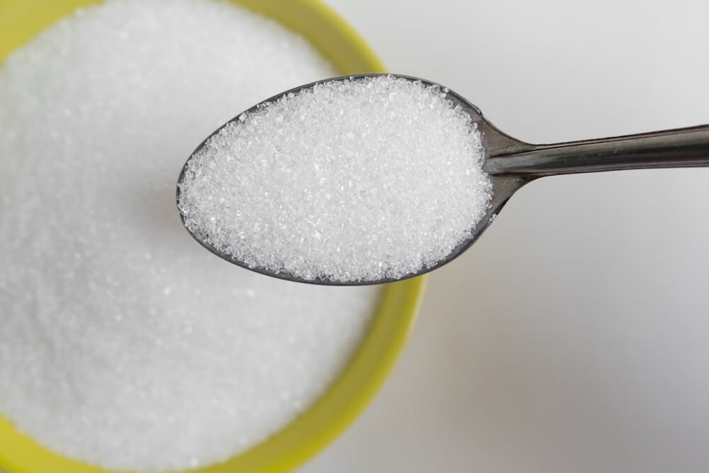 Spooning white sugar out of a yellow bowl