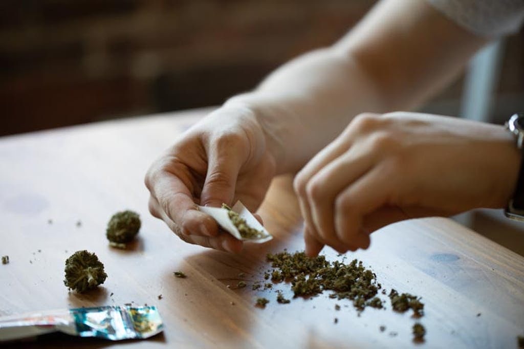 Homem prepara baseado com maconha moída.