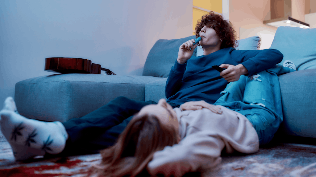 Young creative guy smoking marijuana from a vape pen or vaporizer while relaxing